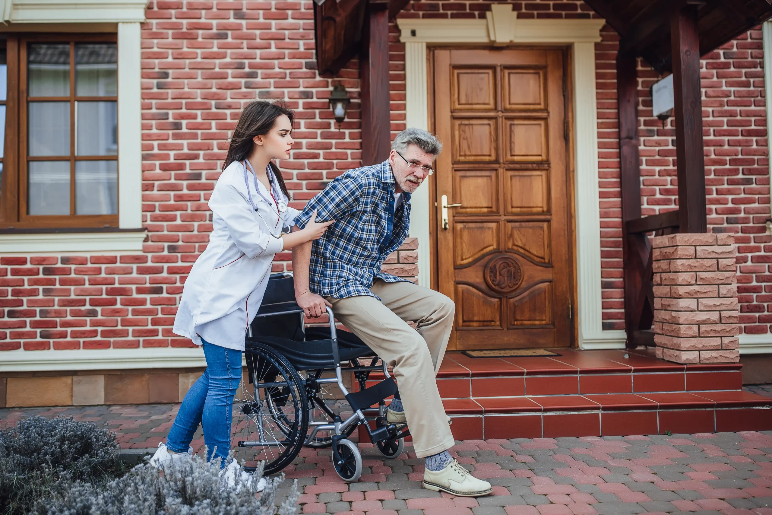 A man pushes a wheelchair while a woman stands beside him, both engaged in conversation outdoors.