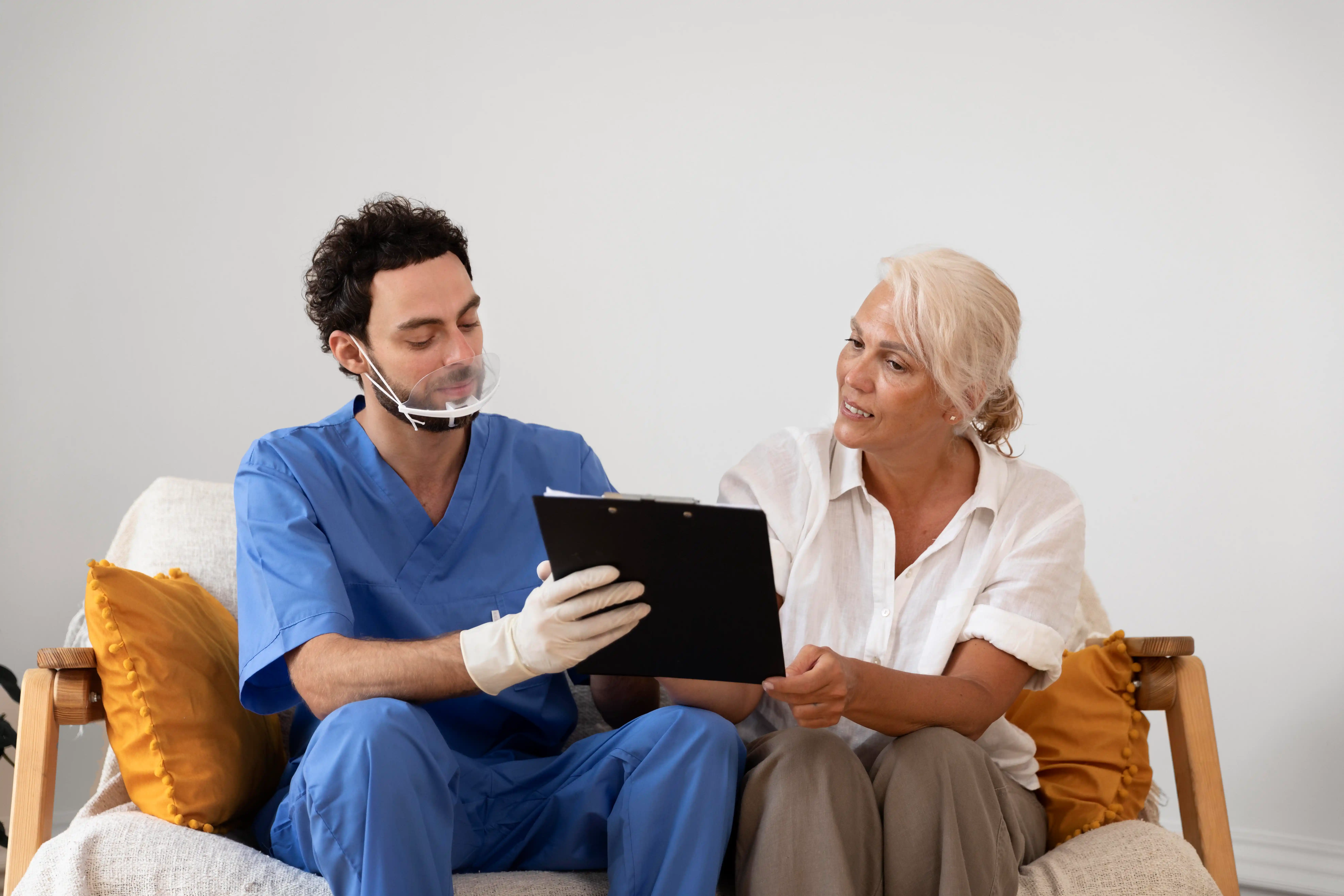 A man and woman sit on a couch, reviewing notes on a clipboard together.