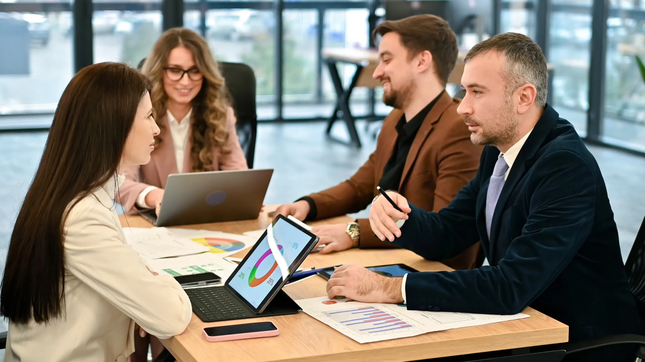 A group of business professionals seated at a table, each using laptops for a collaborative meeting.