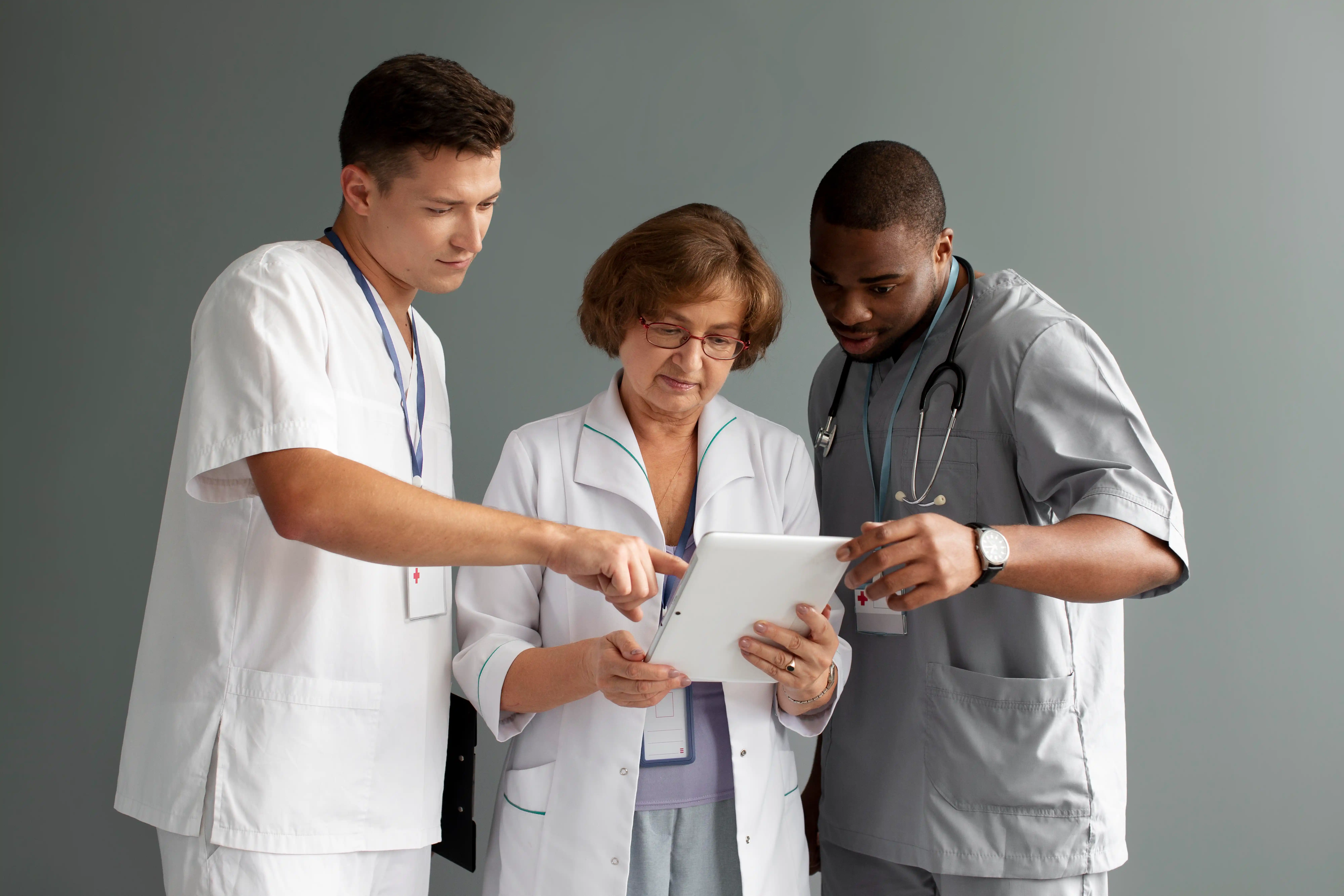 Three medical professionals engaged with a tablet computer, reviewing information and collaborating on patient care.