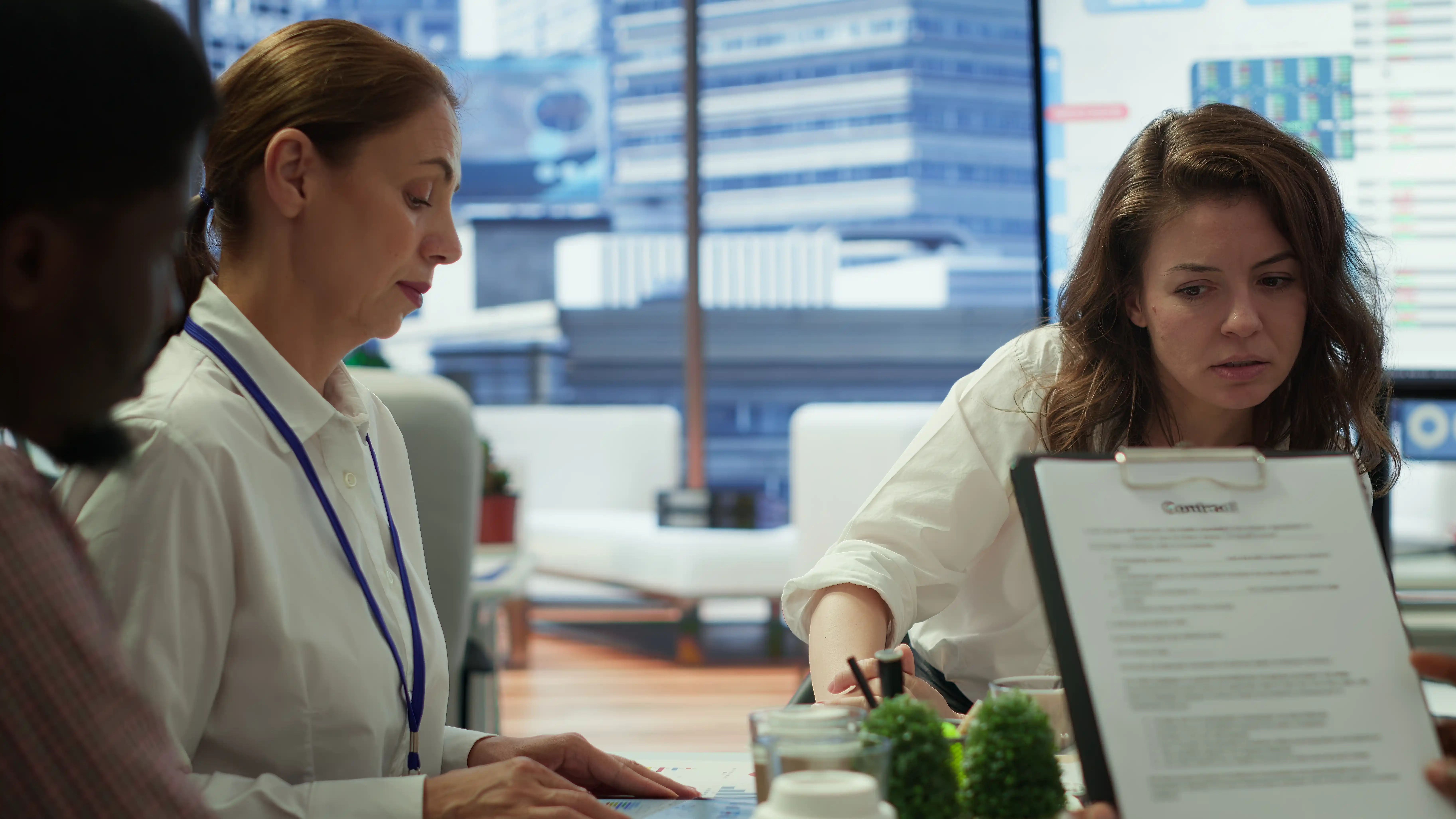 A group of professionals in an office engaged in discussion, with a focus on a document. The setting conveys a collaborative, focused atmosphere.